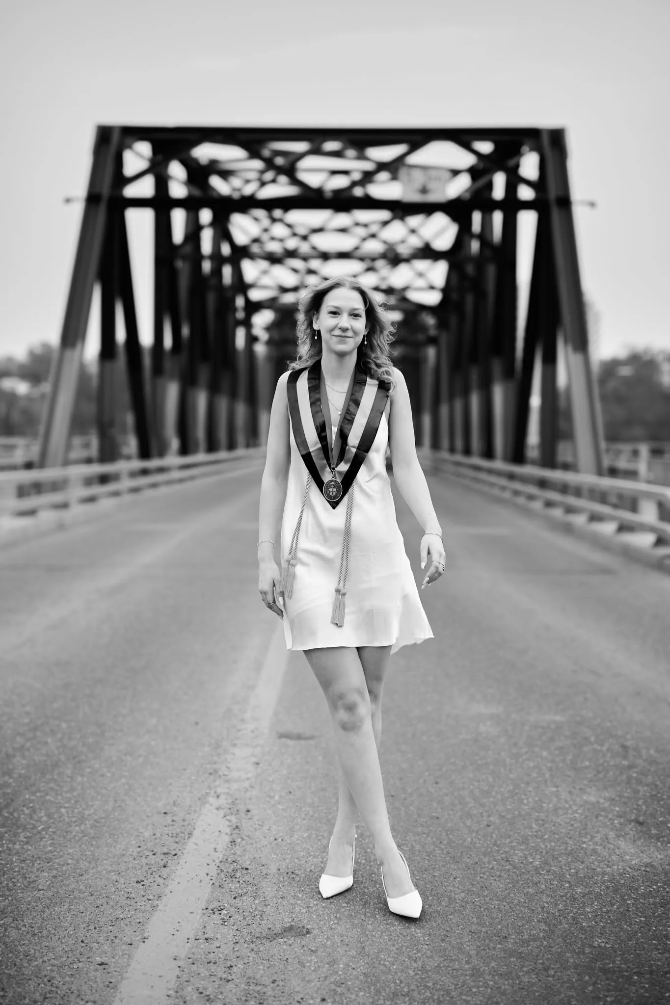Black and white portrait of a woman in an evening gown on a steel bridge