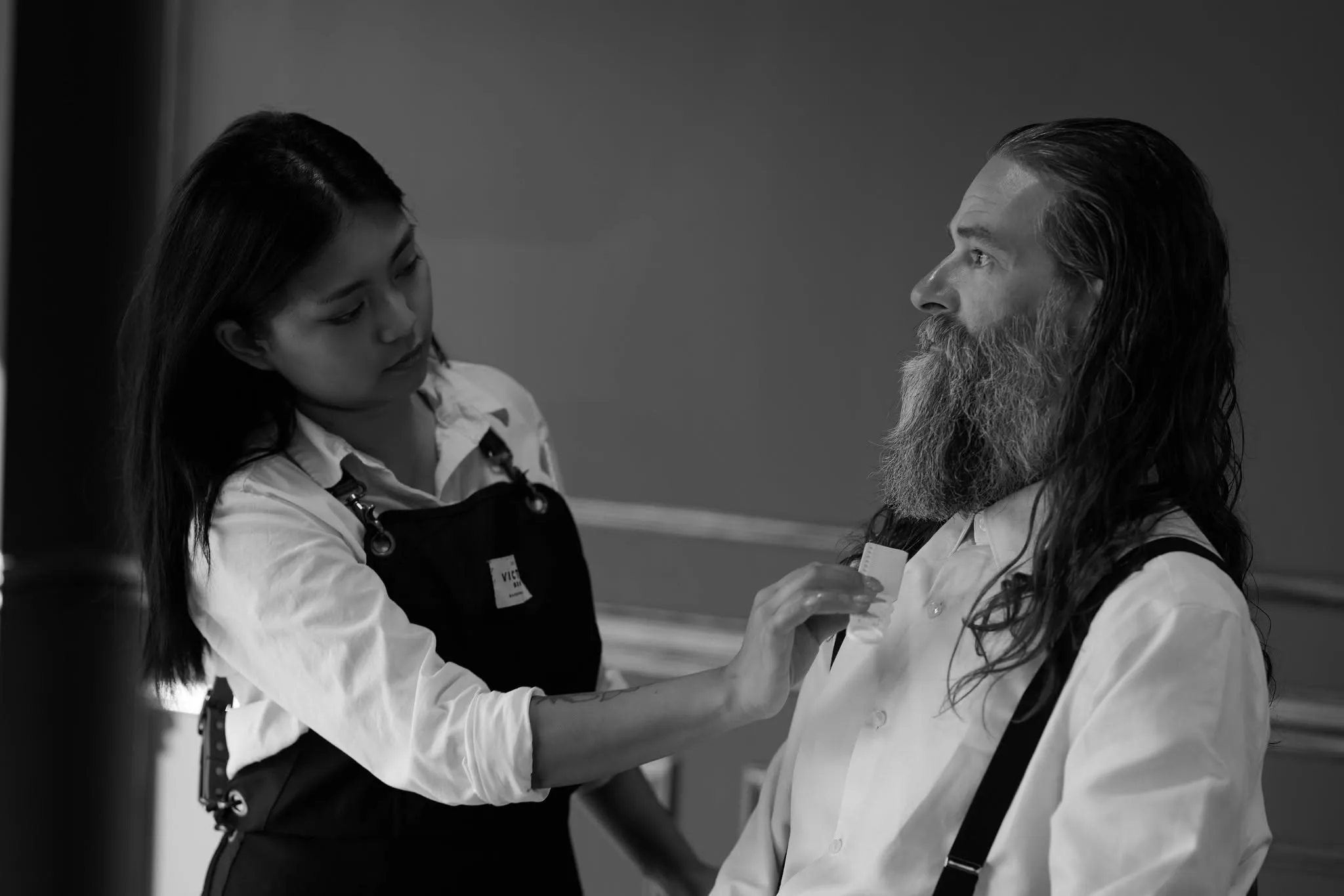 A young girl adjusting the collar of a bearded man in a barbershop
