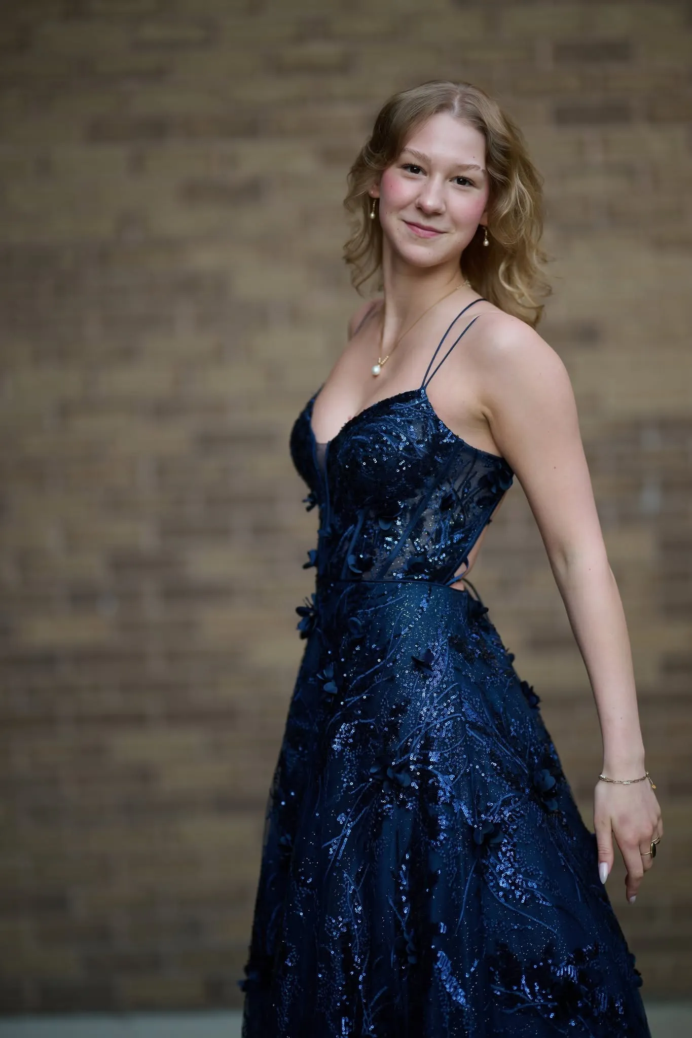 Woman in a navy sequined gown by a brick wall